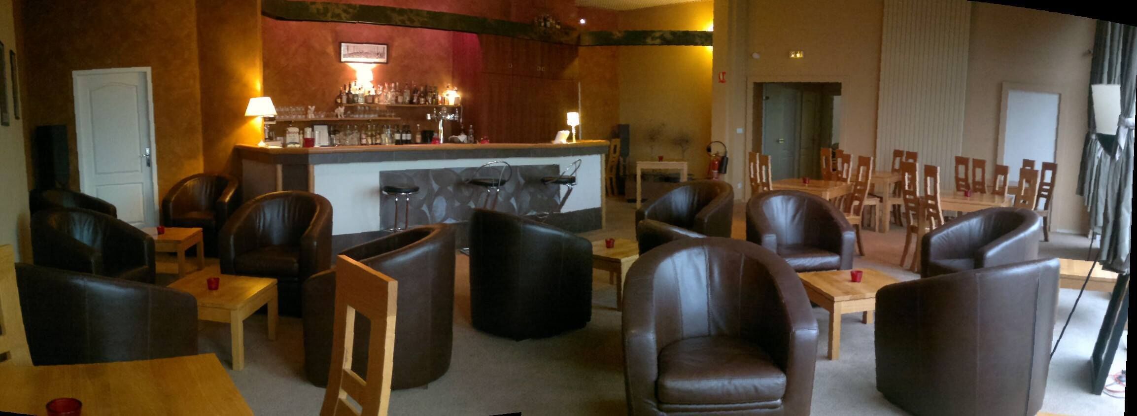 Zona de bar con mostrador y taburetes, rodeada de sillones y mesas de cuero.
