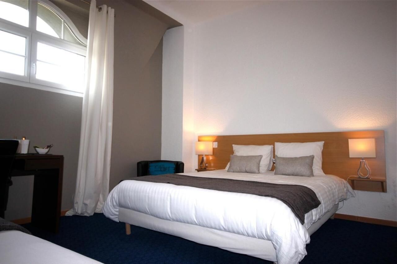A hotel room with a large bed, two bedside lamps, a nightstand, a desk, and a window with curtains.