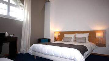 A hotel room with a large bed, two bedside lamps, a nightstand, a desk, and a window with curtains.