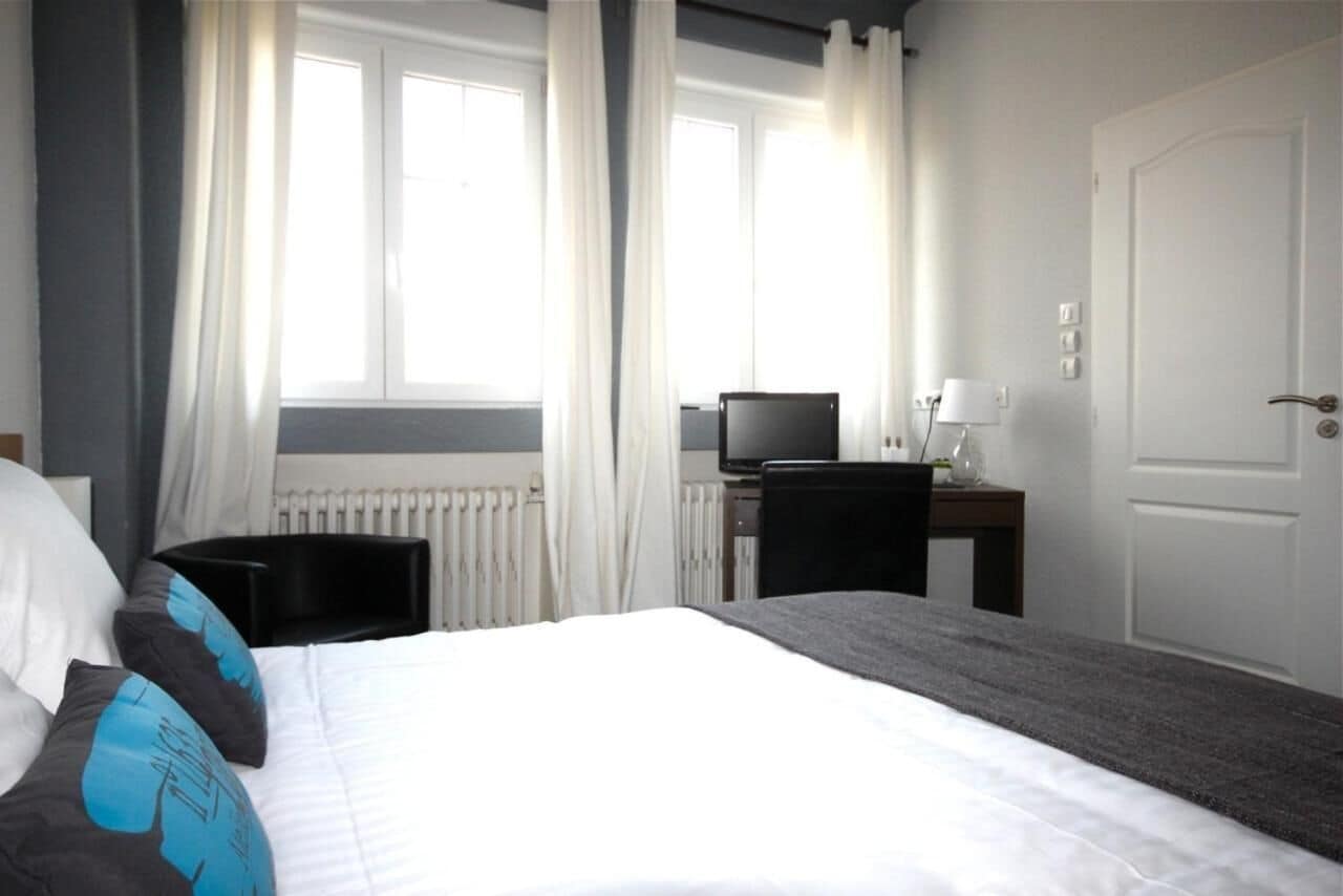 A hotel room with a bed, a desk with a computer, a chair, and a door.
