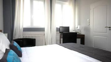 A hotel room with a bed, a desk with a computer, a chair, and a door.