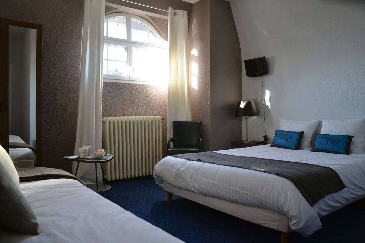 A hotel room with a large bed, a smaller bed, a desk with a chair, a TV, and a window with curtains.