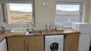 A compact kitchen with a washing machine, a toaster, a kettle, and a sink. - UIST Travel Accommodation (South Uist)