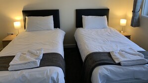 Two single beds with white linens, dark headboards, and bedside lamps. - UIST Travel Accommodation (South Uist)