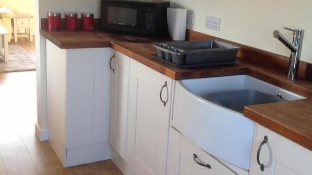 A kitchen with white cabinets, a microwave, and a sink. - UIST Travel Accommodation (South Uist)