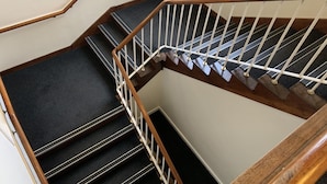 A wooden staircase with a white handrail and black carpeted steps. - UIST Travel Accommodation (South Uist)