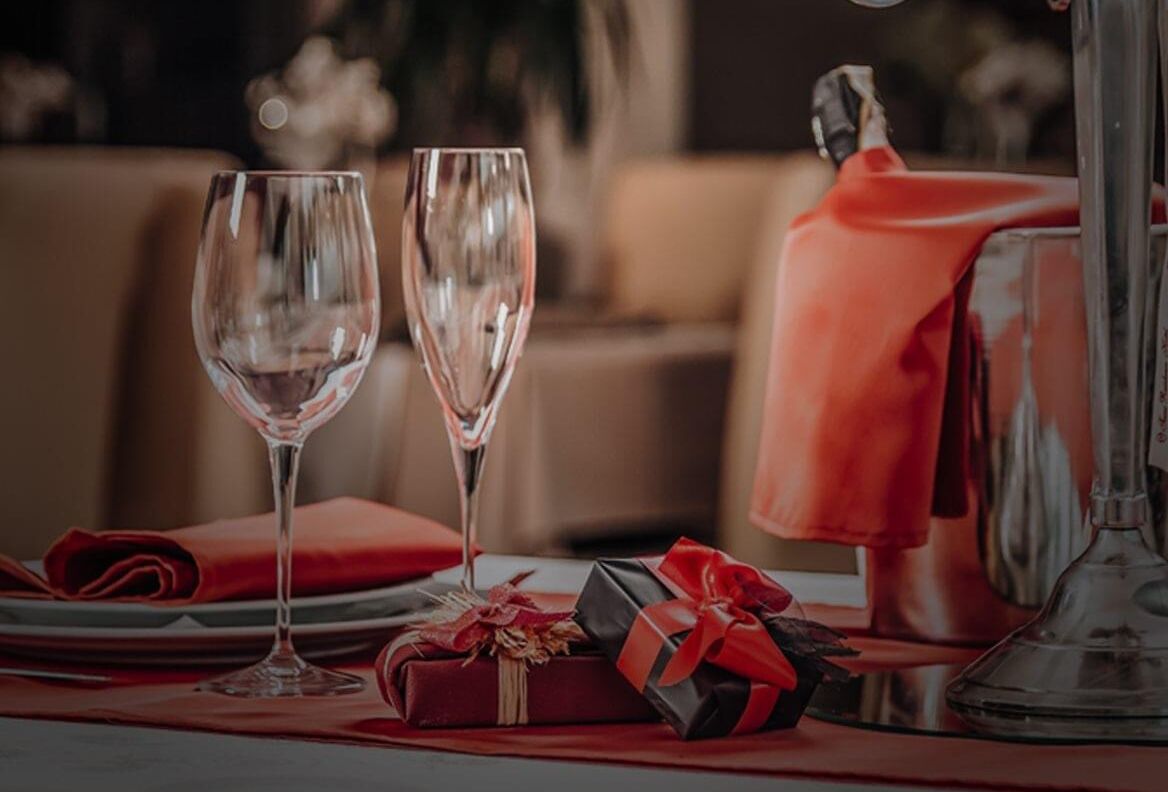 A dining table with two wine glasses, a red napkin, and two gift boxes.