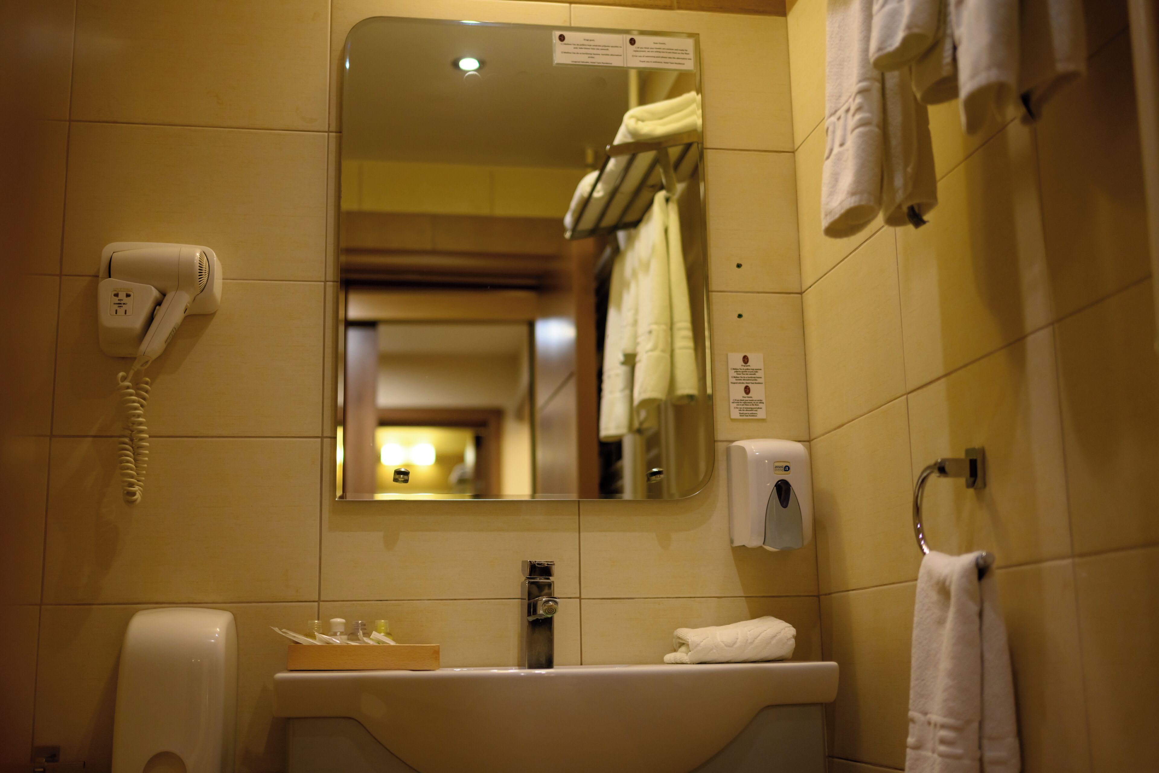 Baño de hotel con lavamanos, espejo, toallero y secador de pelo.