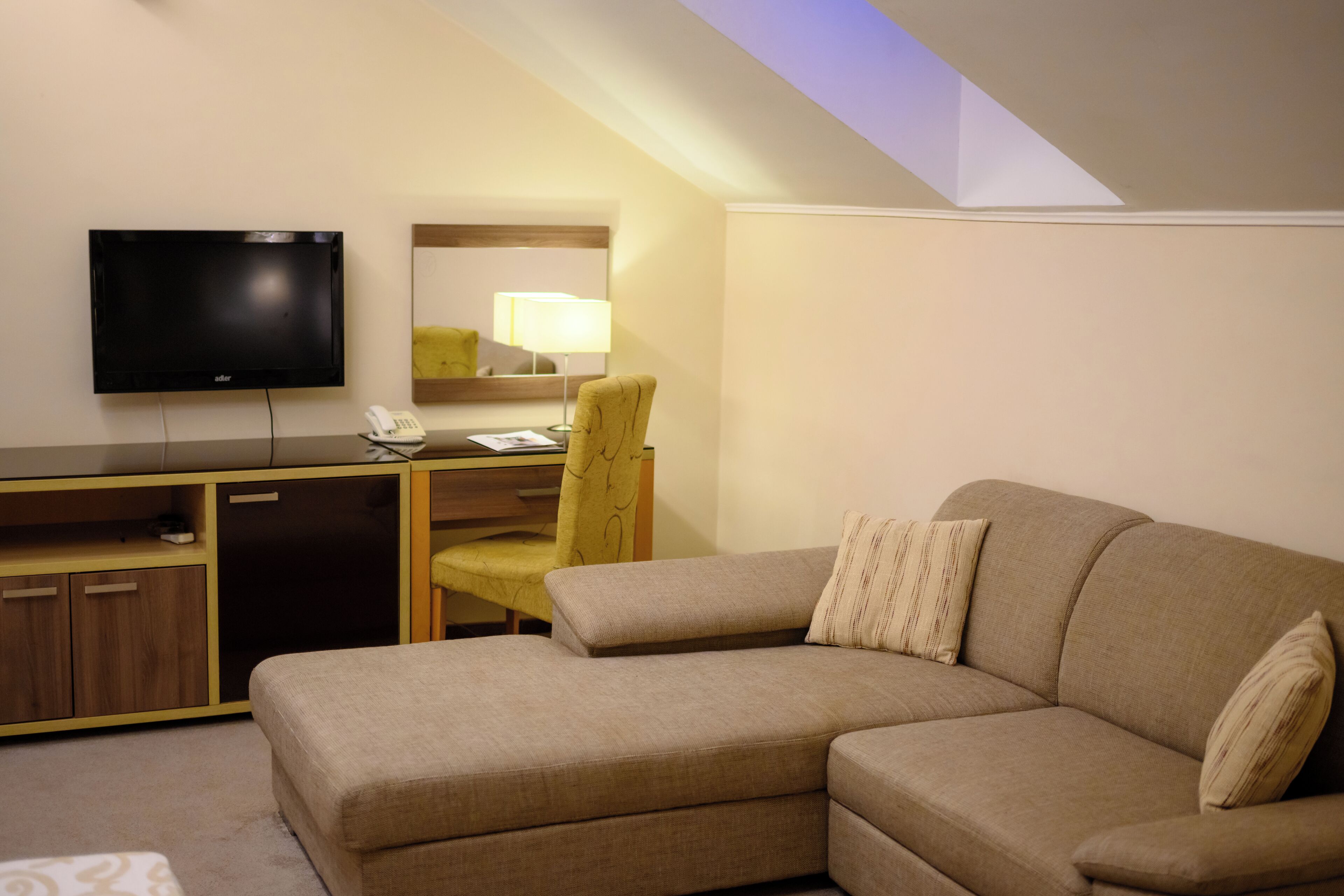 A hotel room with a sofa, a desk with a flat-screen TV, a chair, and a lamp.