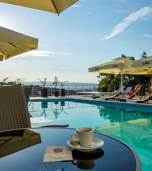 A poolside table with a cup of coffee, a menu, and a view of the pool and lounge chairs.