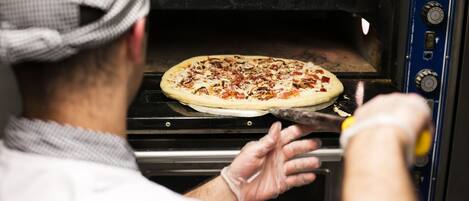 A person in a chef's hat and gloves placing a pizza into a commercial oven.