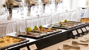 Un bufé con diferentes estaciones de comida, que incluyen ensaladas, frutas y otros platos.