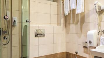 A modern bathroom with a glass-enclosed shower, a toilet, a bidet, and a hairdryer.