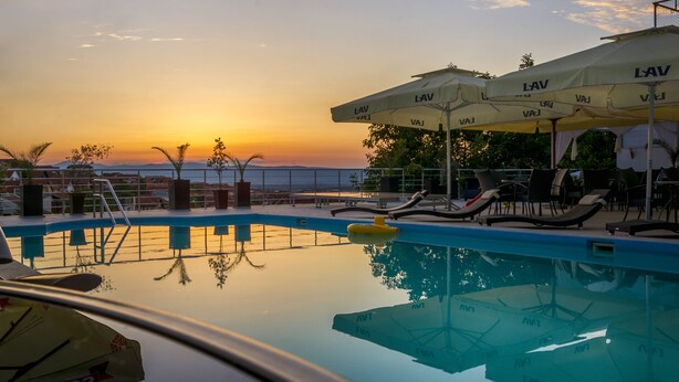 Un área junto a la piscina con sillones y sombrillas, una piscina que refleja el atardecer y vistas al mar.
