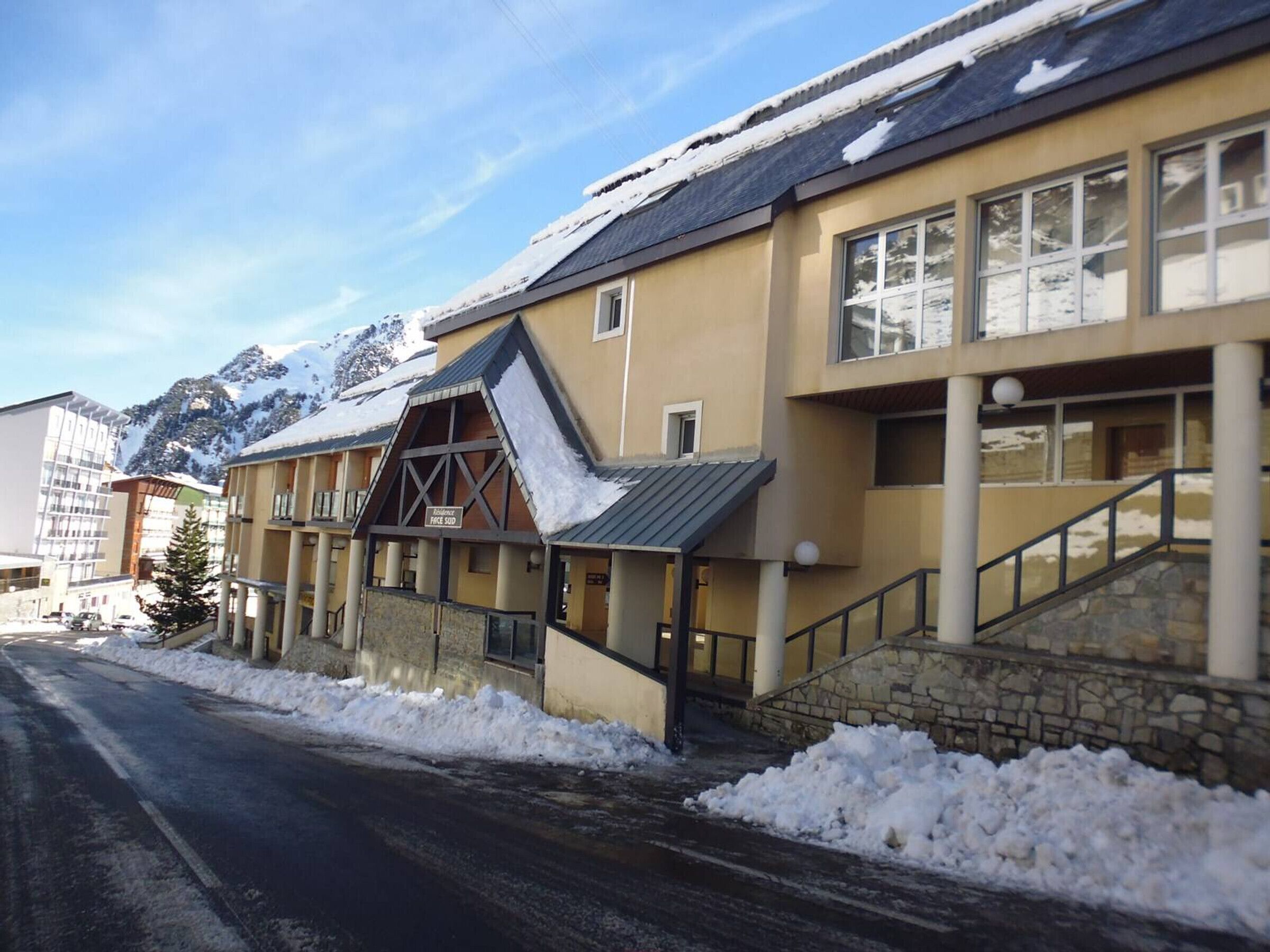 A hotel with a snow-covered roof, a stone staircase, and a mountain backdrop.