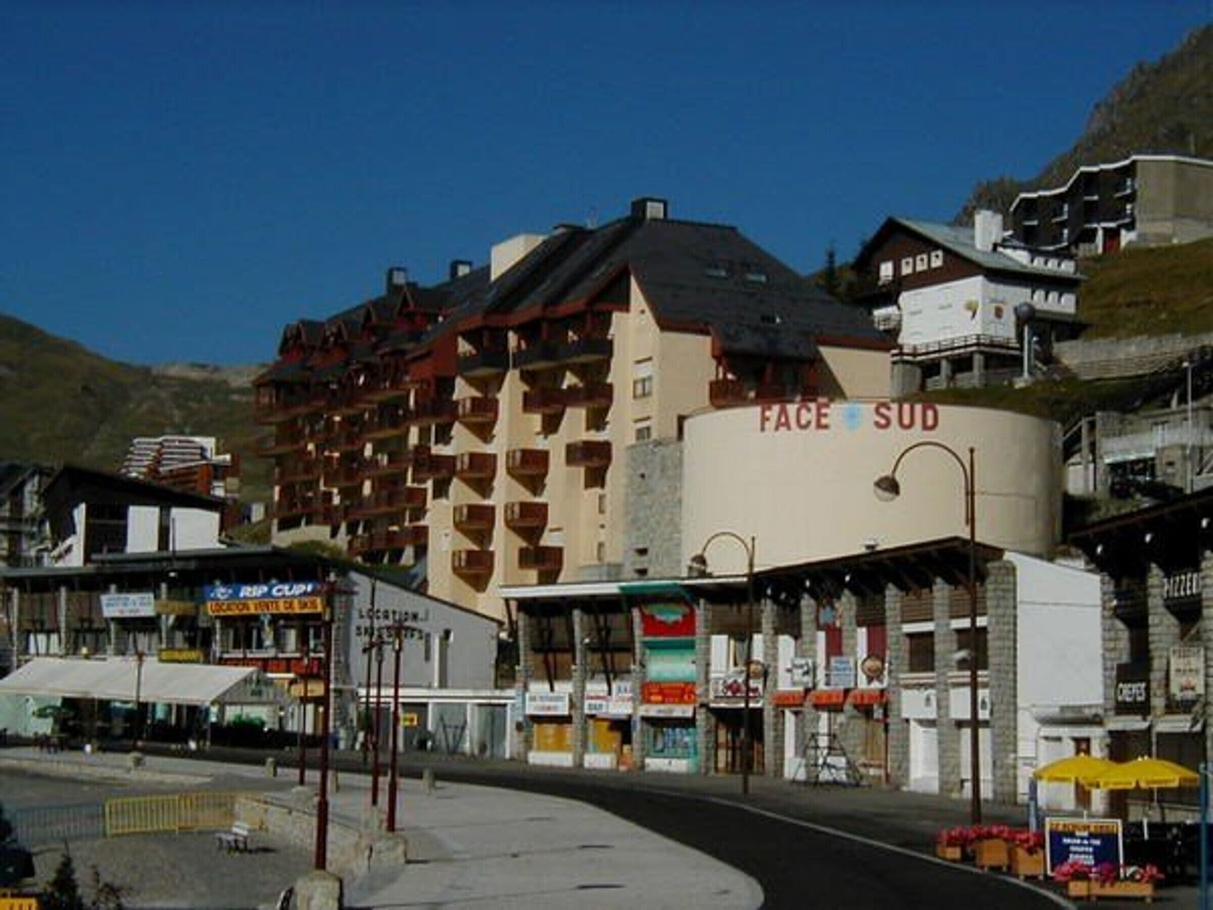 A multi-story hotel with balconies, a sign reading "FACE SUD," and various storefronts in the foreground.