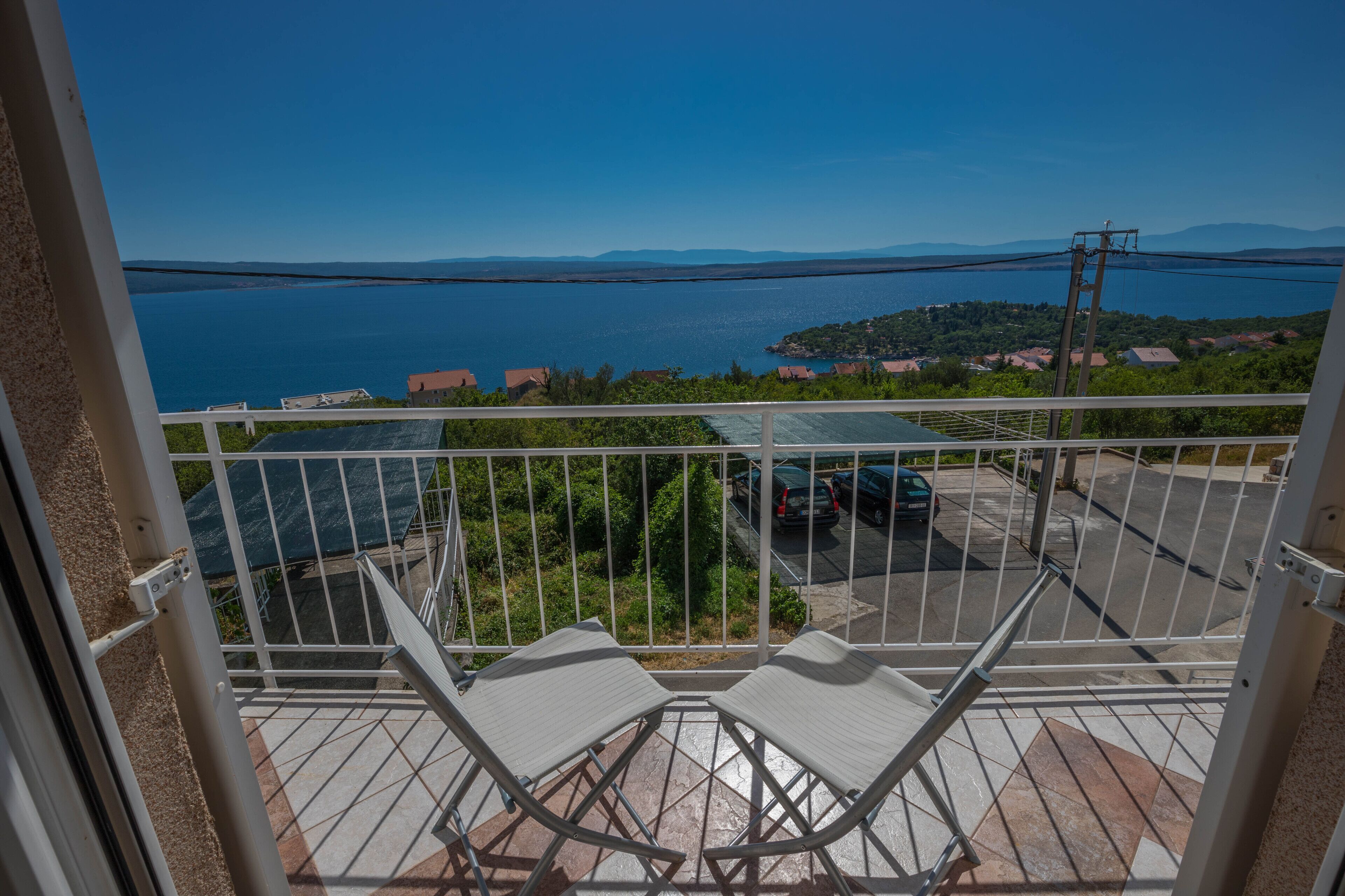 Un balcon donnant sur une étendue d’eau, un espace de stationnement et un paysage lointain.