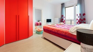 A bedroom with a large bed, a red wardrobe, a desk with a computer, and a window with curtains. - GuestHost - Bright apartment included in a building of very recent construction (Milano)