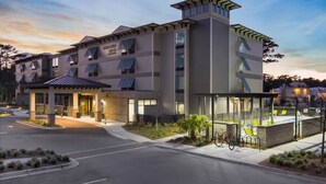 Un hotel de varios pisos con diseño moderno, que cuenta con una entrada cubierta, zona de estar al aire libre y paneles solares.