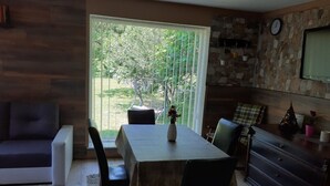 A dining area with a table, chairs, and a vase of flowers. There is a window with a view of greenery outside. - Holiday House Stipe (Bakar)