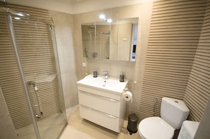 A modern bathroom with a glass-enclosed shower, a white sink with a mirror above it, and a toilet.