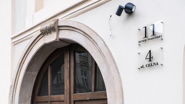 A double wooden door with a stone archway, a white wall with a number plaque, and a brick-paved ground. - Old Town Vistula Premium Apartments (Kraków)