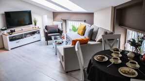 A modern living room with a flat-screen TV, a sofa, a dining table set for tea, and a skylight above. - Old Town Vistula Premium Apartments (Kraków)