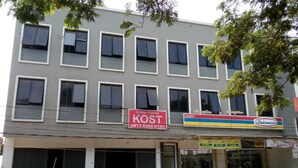 Un edificio con varias ventanas, un letrero que dice 'DISINI TERIMA KOST' en la planta baja, y una tienda 'Indomart' a la derecha.