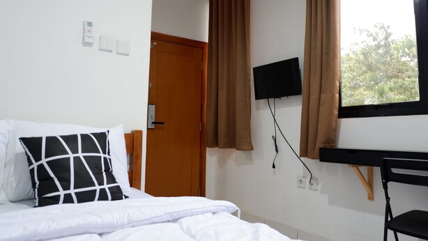 Habitación de hotel con cama, televisión montada en la pared, ventana con cortinas y puerta.