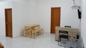 Una habitación con una mesa de madera, un banco y dos sillas. Hay dos puertas de madera y una pared blanca.