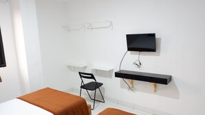 Una habitación con dos camas, un escritorio, una silla, un televisor y una estantería.
