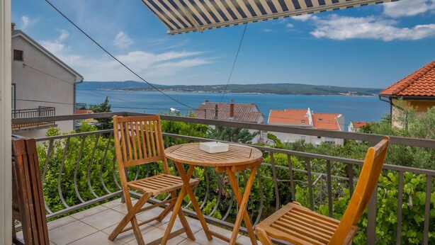 A balcony with two wooden chairs and a small table, overlooking a coastal view with houses and a clear sky. - Apartment Maro (Crikvenica)