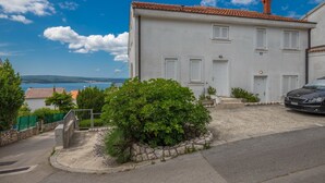 A two-story building with a white facade and red-tiled roof, a stone staircase leading to the entrance, and a view of the sea in the background. - Apartment Maro (Crikvenica)
