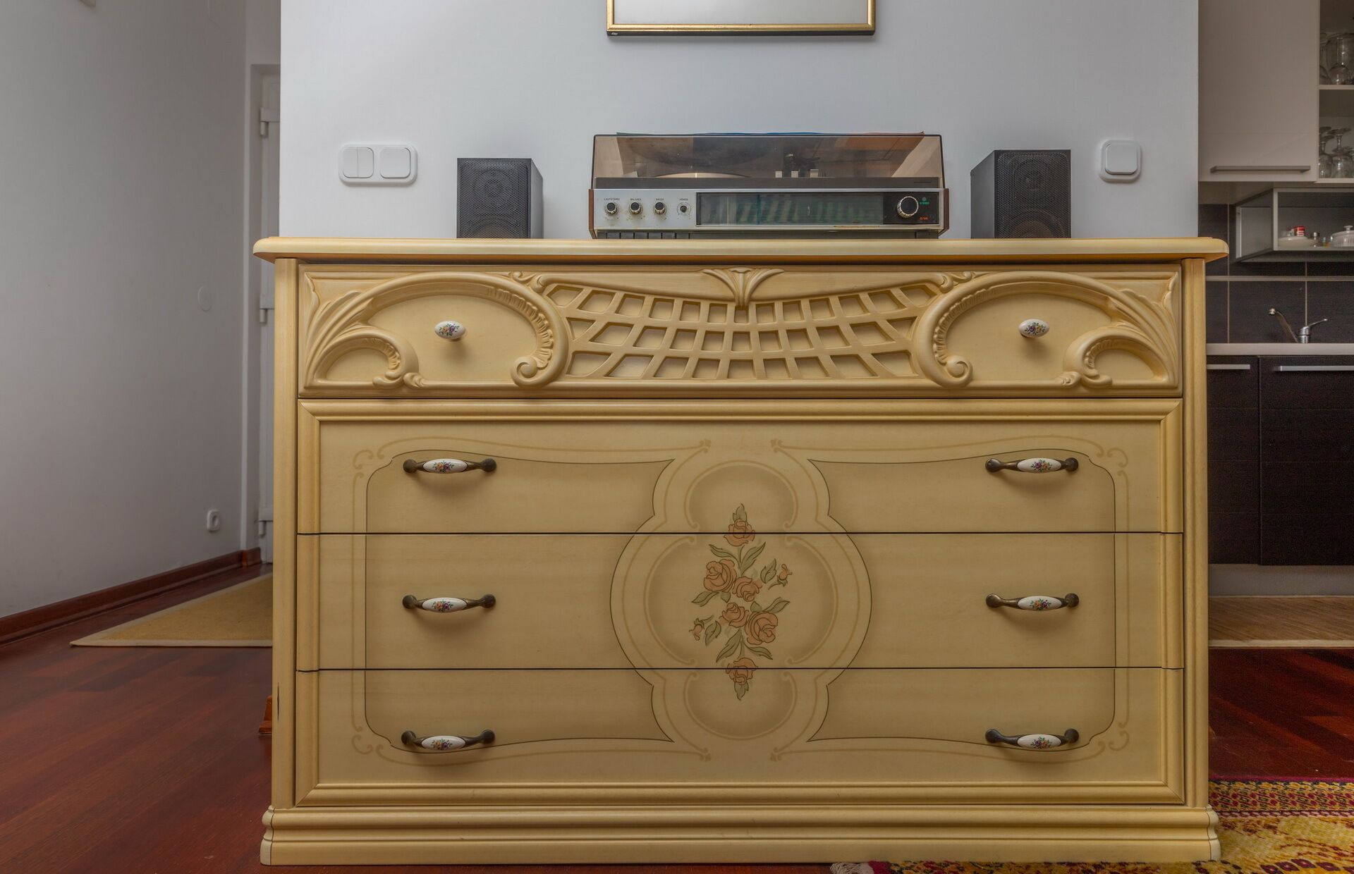 Un aparador color crema con detalles florales tallados y una radio encima.