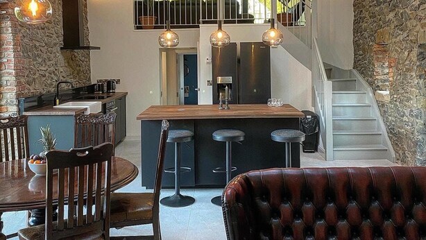 A modern kitchen with a central island, a dining area with a wooden table and chairs, and a staircase leading to an upper level. - The Old Bushmills Barn (Bushmills)