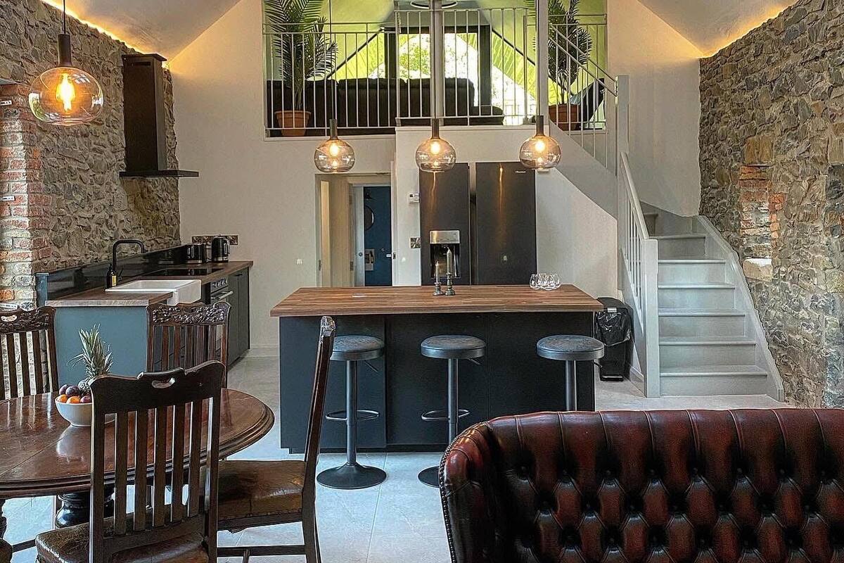 A modern kitchen with a central island, a dining area with a wooden table and chairs, and a staircase leading to an upper level.