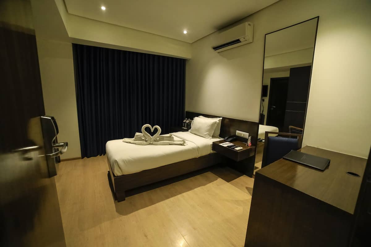Una habitación de hotel con una cama, un escritorio, una silla, un espejo y un televisor.