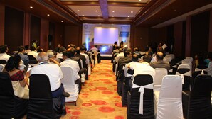 A conference room with rows of chairs facing a stage with a presentation screen. - Hotel German Palace (Gandhinagar)