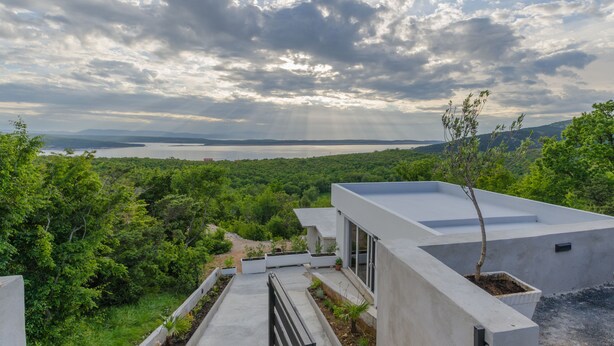 A modern building with a flat roof, surrounded by lush greenery and overlooking a body of water. - Holiday House Linda (Crikvenica)