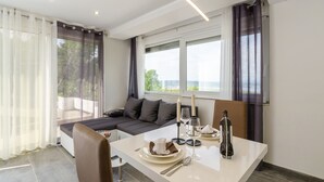 A modern room with a dining table set for two, a sofa, and a large window offering a view. - Holiday House Linda (Crikvenica)