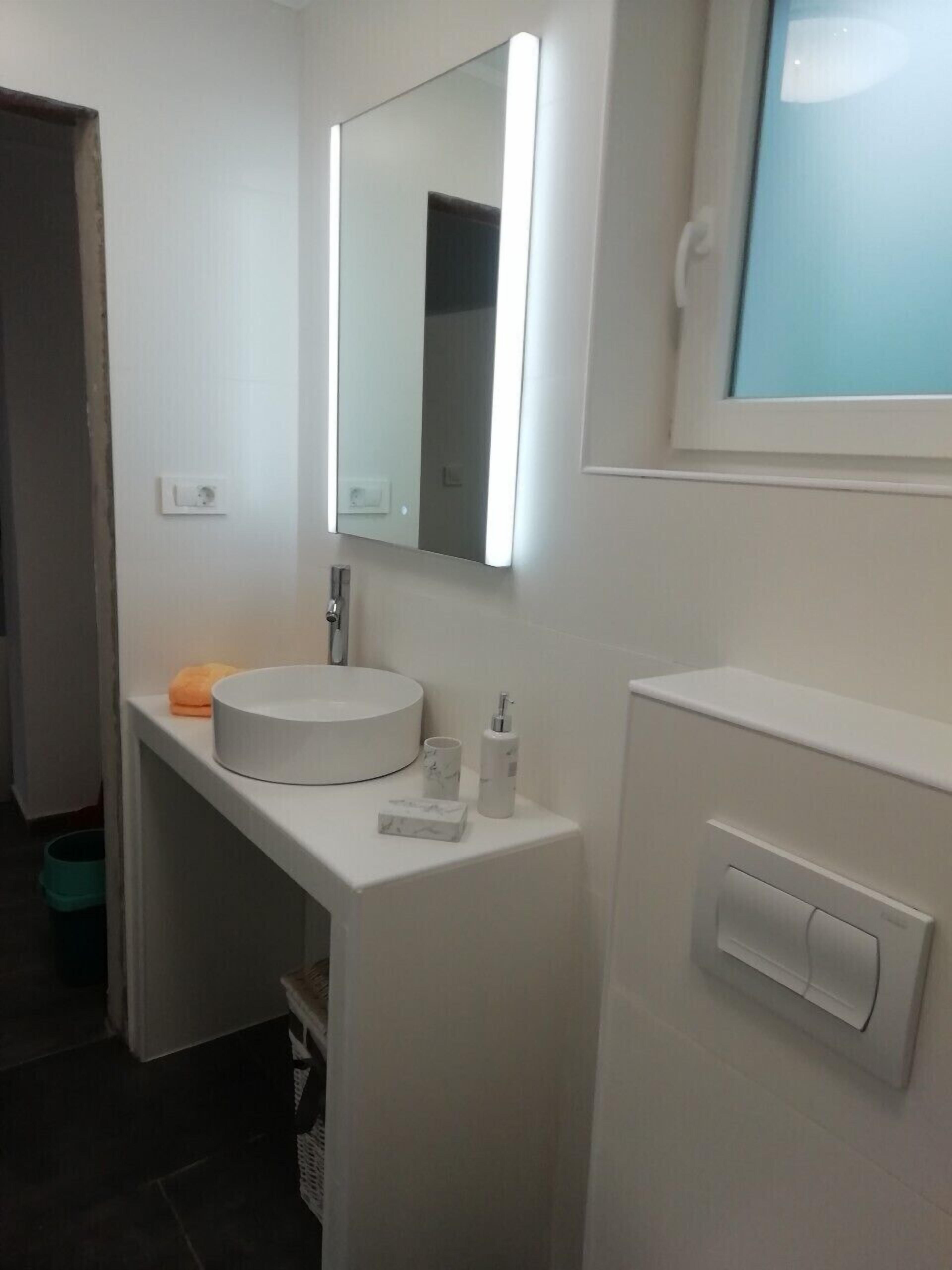 Une salle de bain moderne avec un lavabo blanc, un miroir et une fenêtre.