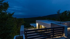 A modern building with a flat roof, surrounded by greenery, and overlooking a body of water. - Holiday House Linda (Crikvenica)