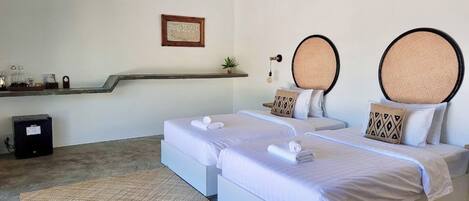 A hotel room with two beds, a small desk, a shelf with items, and a framed picture on the wall.