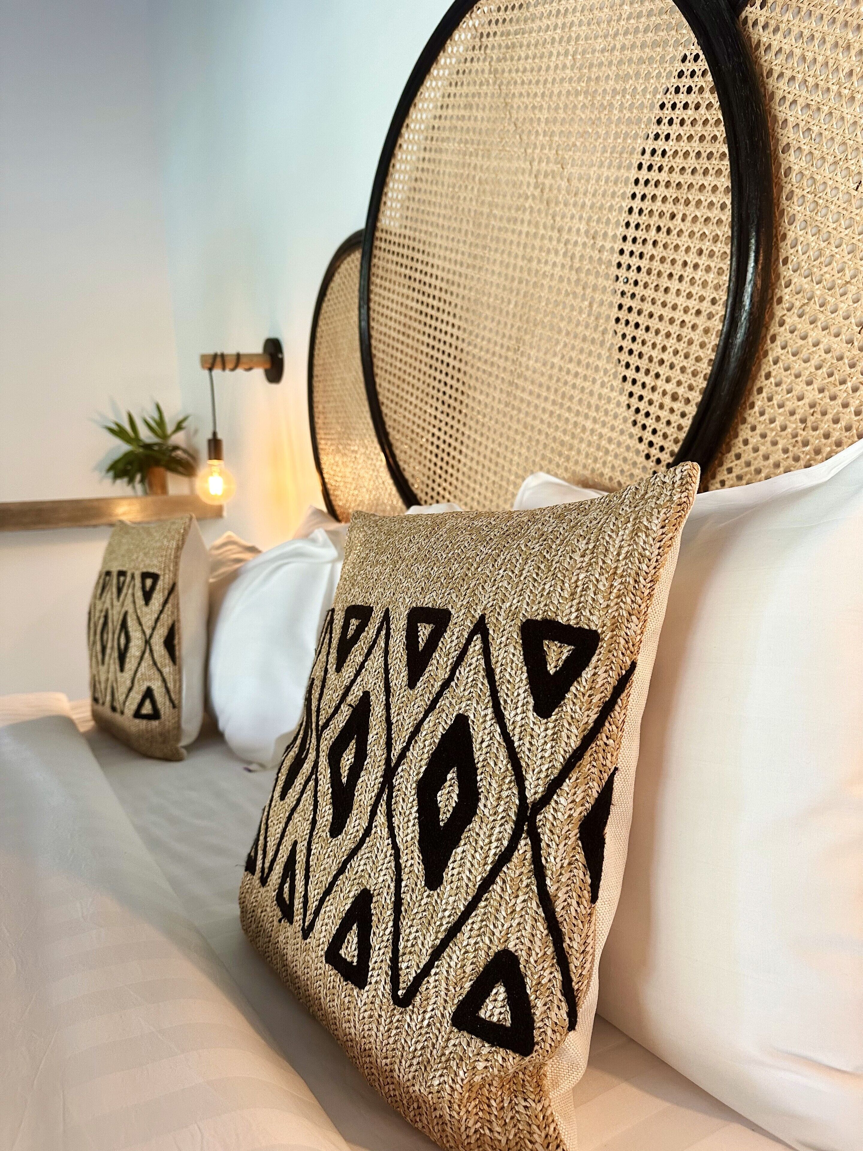 A bed with white linens, a woven headboard, and decorative pillows with geometric patterns.