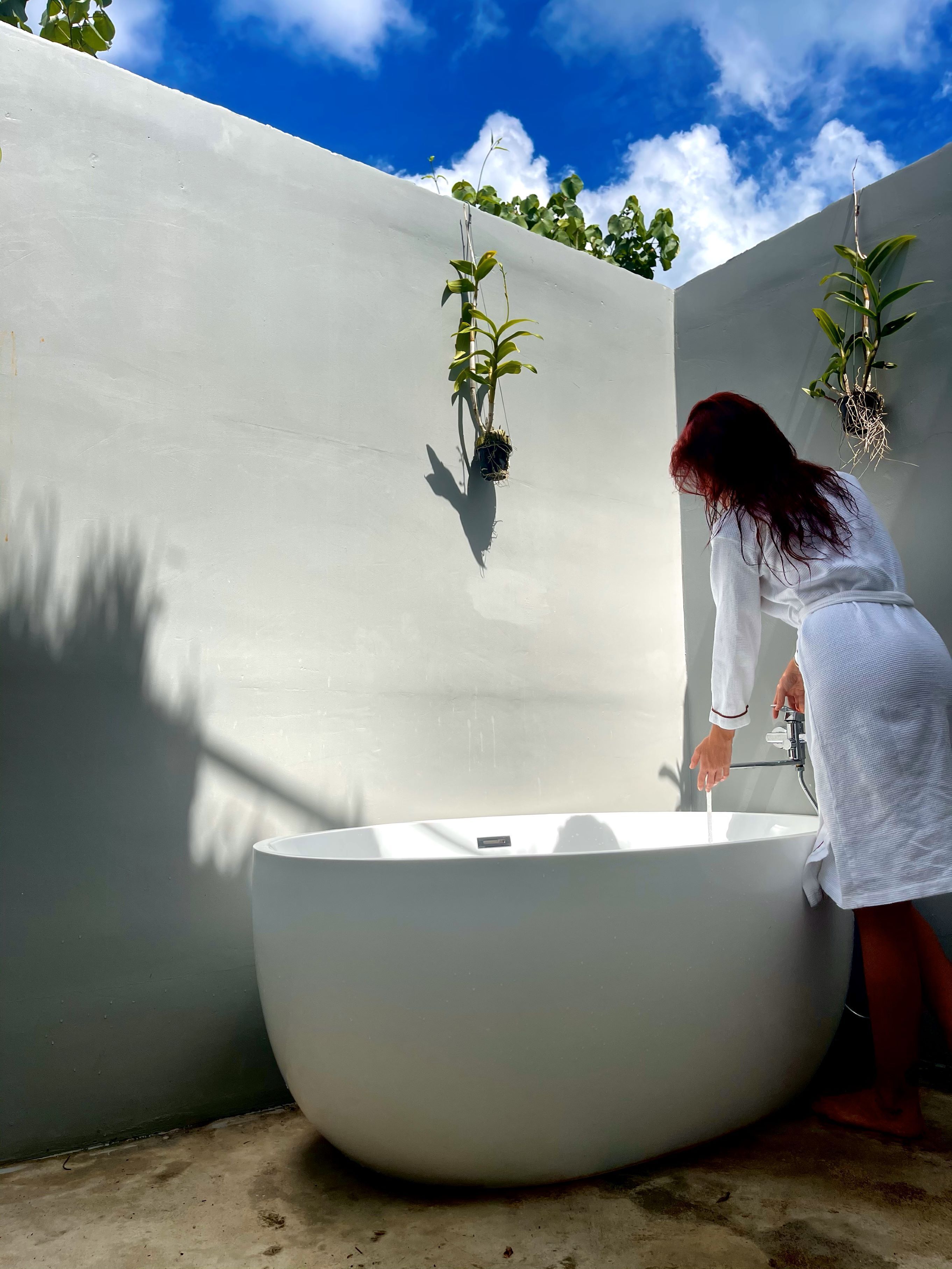 A woman in a white robe using a modern, large bathtub.