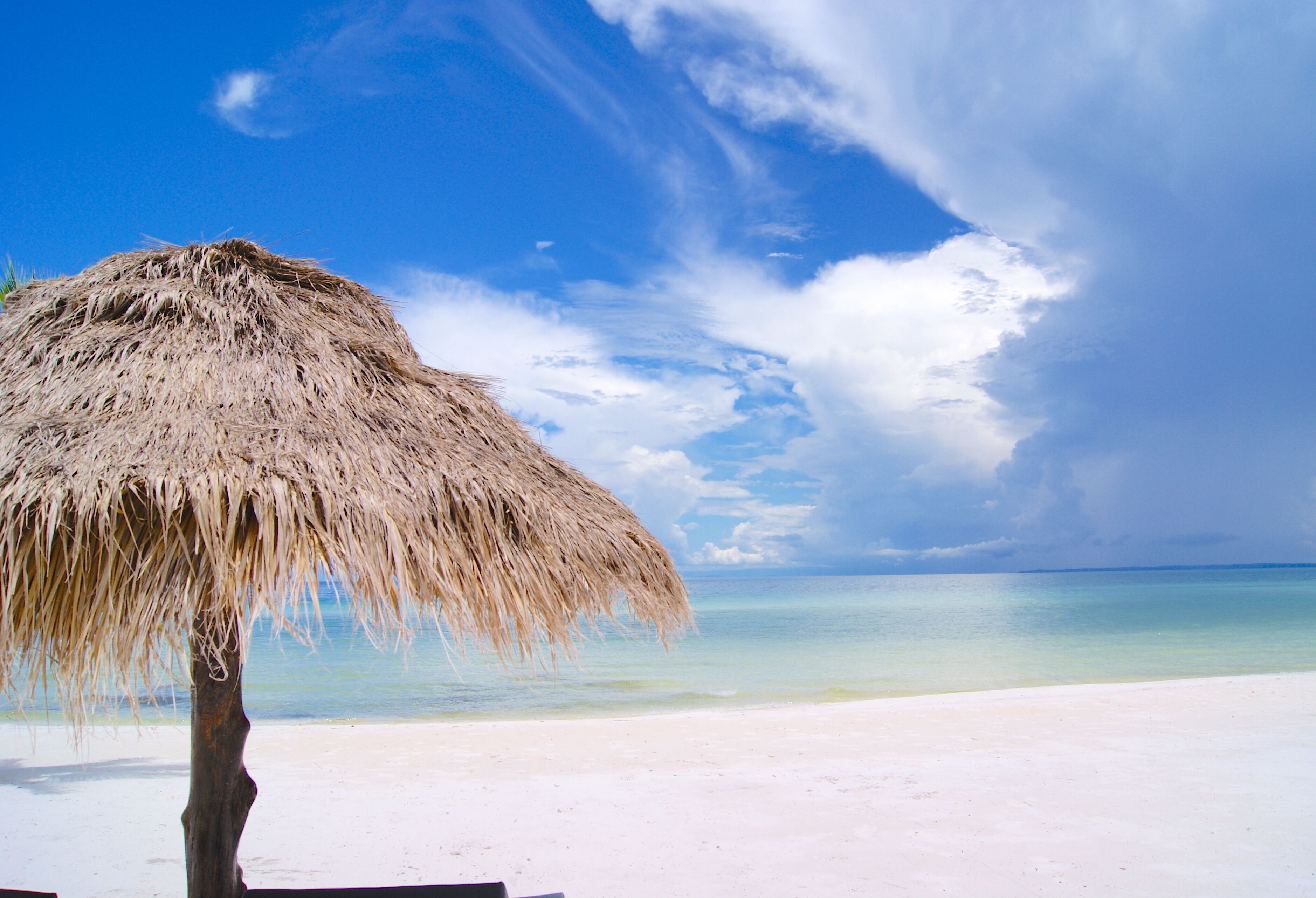 A beach with a thatched umbrella and a clear view of the ocean.