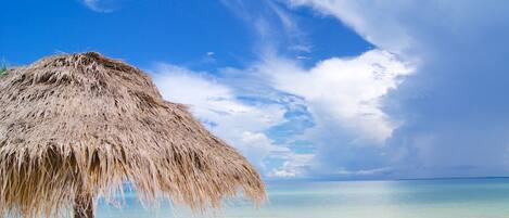 A beach with a thatched umbrella and a clear view of the ocean.