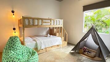 A bunk bed room with a woven rug, a green bean bag chair, a tent, and a window with a view of greenery.