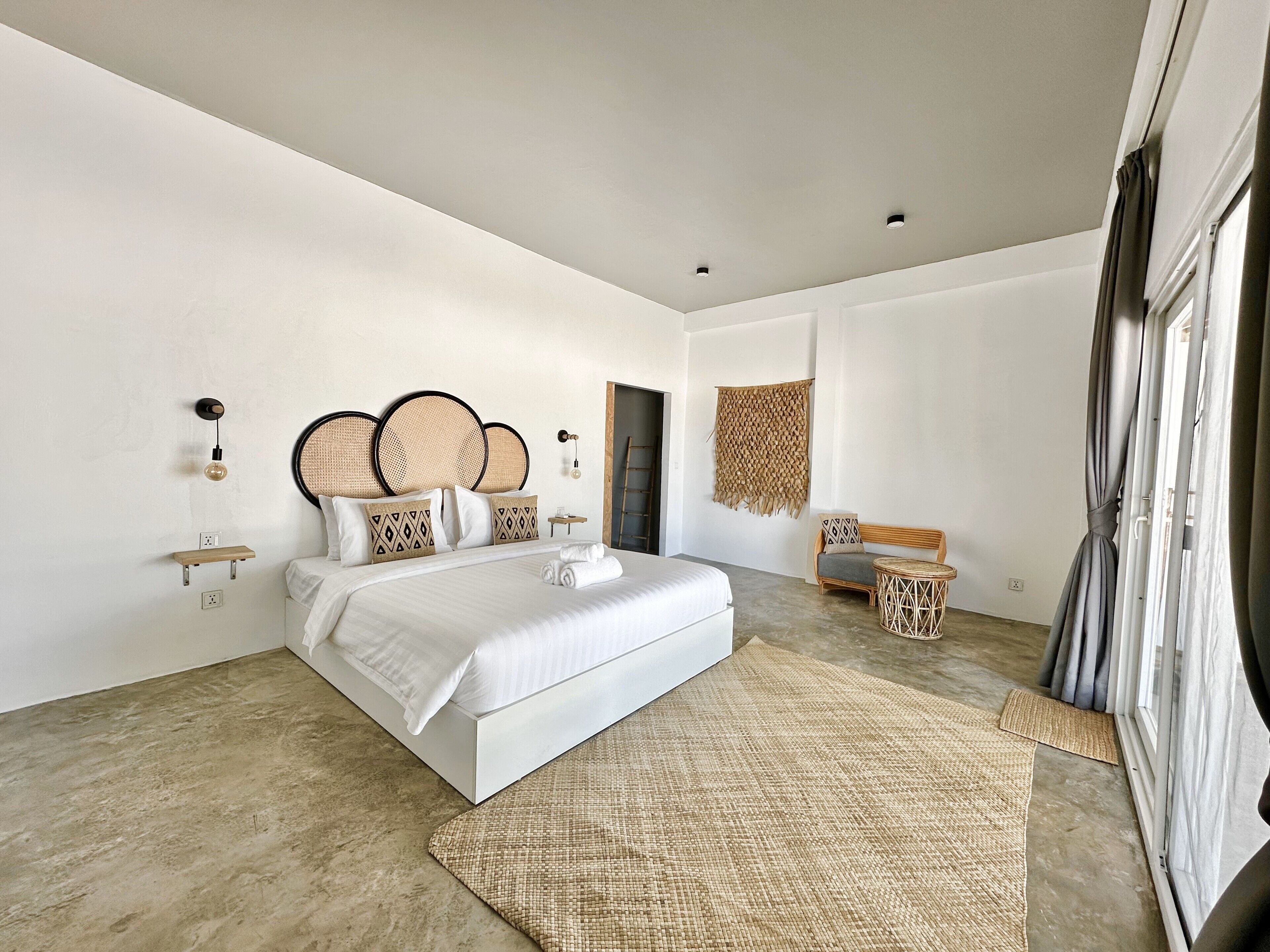 A modern bedroom with a large bed, a small seating area, and a view of the outdoors.