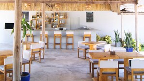 A spacious indoor area with wooden tables and chairs, a thatched roof ceiling, and a bar area with shelves of bottles. - The Secret Garden Koh Rong (Koh Rong)